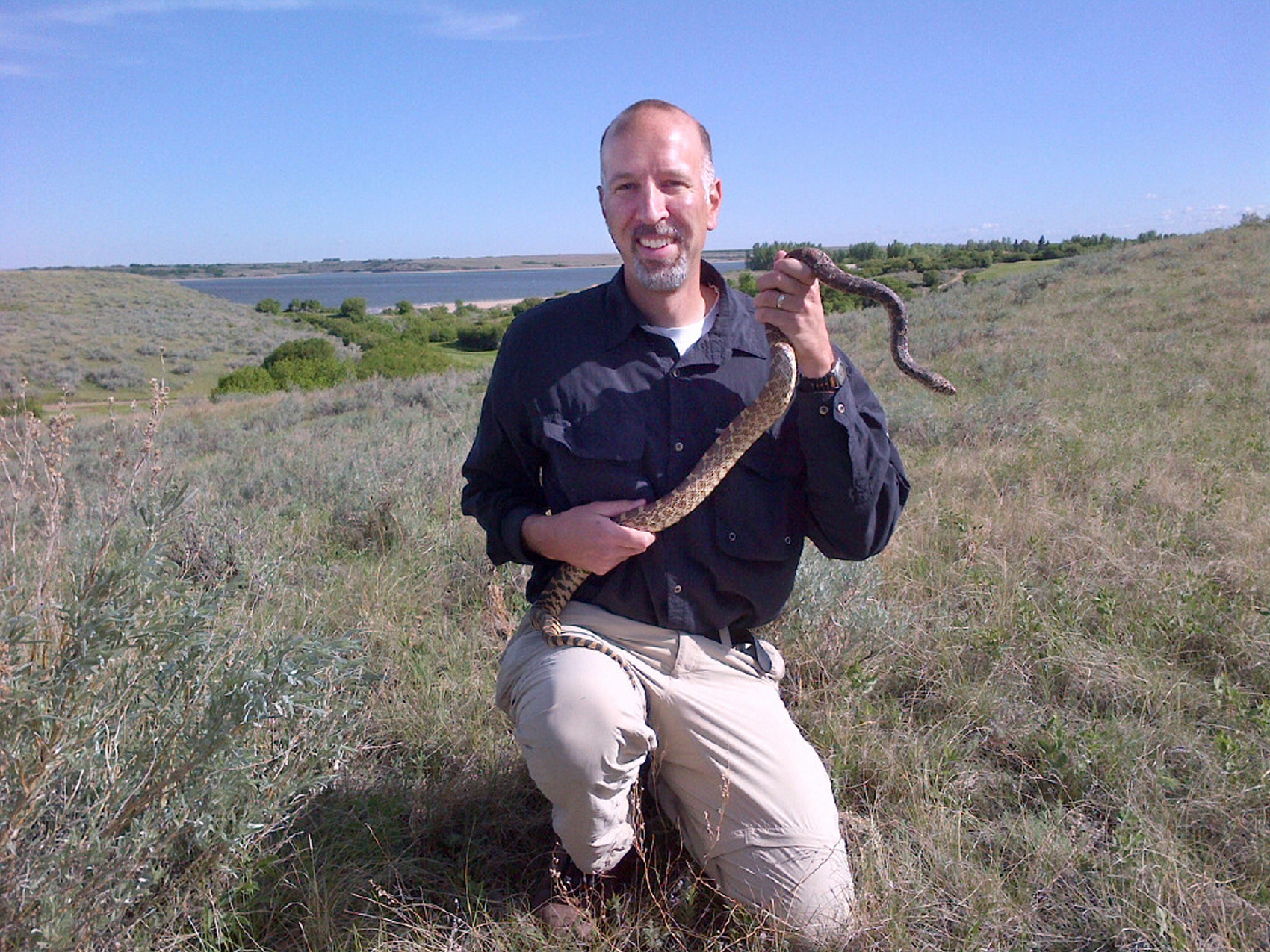 Chris Somers kneels with a bullsnake in his hand.